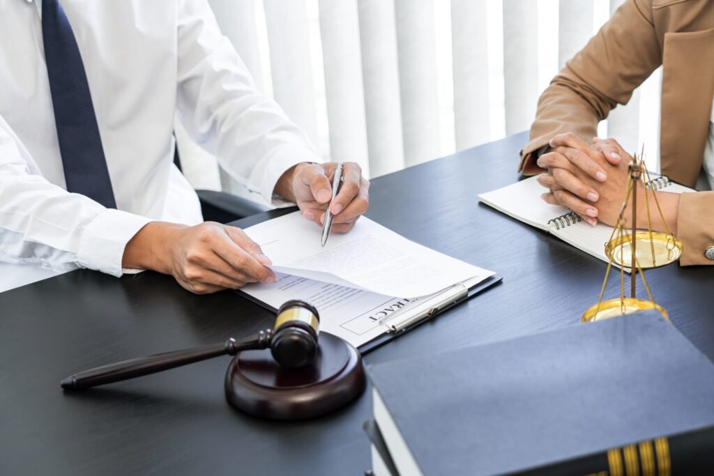 Abogados en seguros de gastos médicos en oficina analizando contrato con un cliente, junto a mazo y balanza.