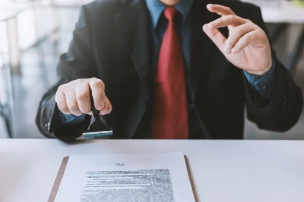Toma visual de hombre trajeado poniendo sello a un permiso de uso a la person que hizo caso a cómo proteger legalmente tu negocio desde el inicio